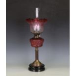 An early 20th century brass and cranberry glass oil lamp with foliate etched glass shade above a