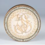 A late 18th century gold mounted circular snuff box, the glazed lid with scrolling hairwork initials