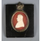 An early 19th century miniature wax portrait of a gentleman, within an ebonized rectangular wooden