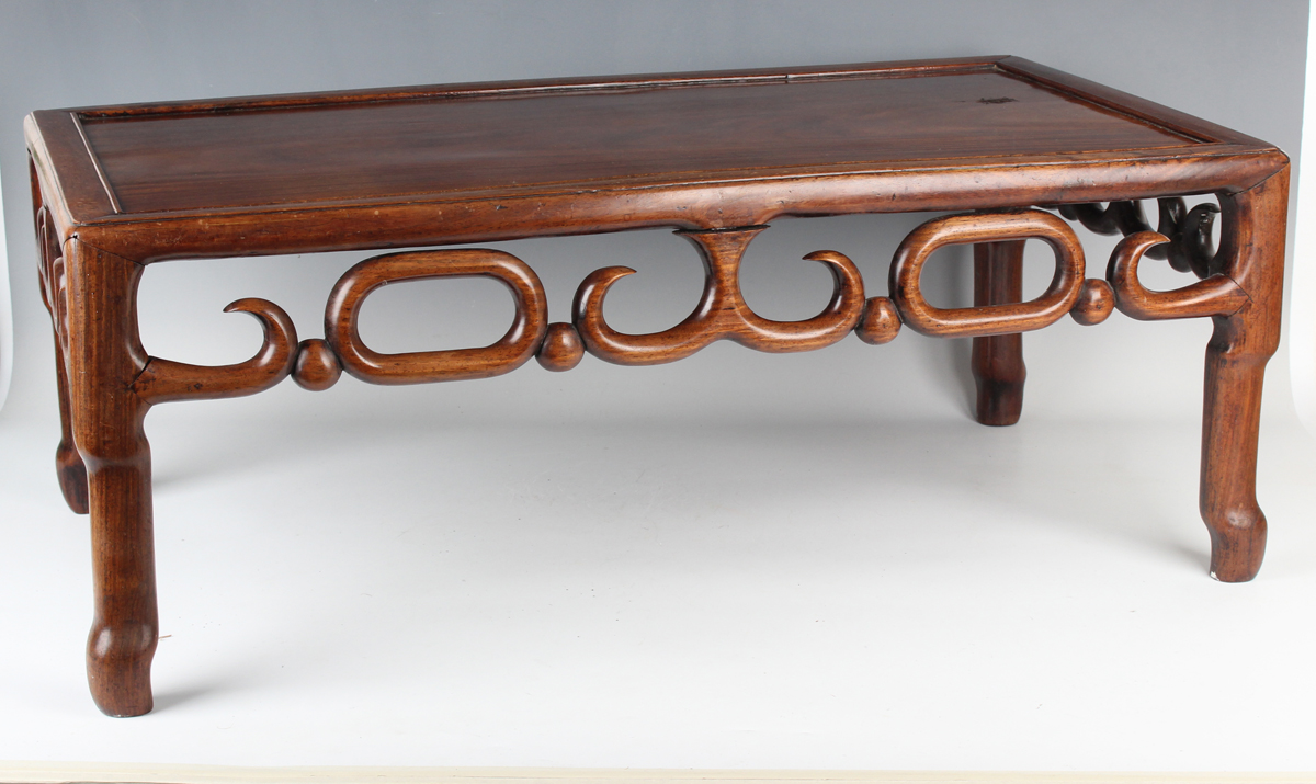 A Chinese hardwood low table, early 20th century, the rectangular panelled top above a carved and