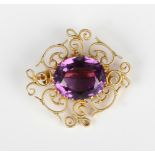 A gold and amethyst single stone brooch, claw set with the oval cut amethyst in a cannetille work