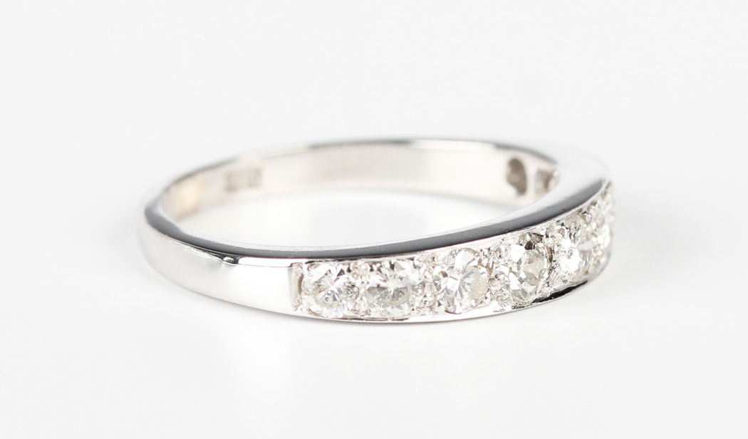 A white gold and diamond nine stone half-hoop eternity ring, mounted with a graduated row of
