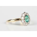 A gold, emerald and diamond oval cluster ring, collet set with the oval cut emerald within a