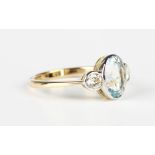 A gold ring, collet set with an oval cut aquamarine between two collet set circular cut diamonds,