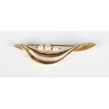 A gold and cultured pearl bar brooch in a curved design, mounted with three cultured pearls,