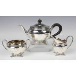 A George V silver three-piece tea set of circular faceted form, on reeded scroll legs, comprising