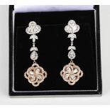 A pair of two colour gold and diamond pendant earrings, each with a quatrefoil shaped drop,