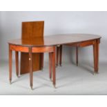 A George III mahogany D-end dining table with central drop-flap section, raised on brass caps and