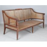 A George III mahogany framed bergère settee, the moulded frame with carved scroll handrests, on