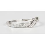 A white gold and diamond oval hinged bangle, the front in a crossover design, mounted with