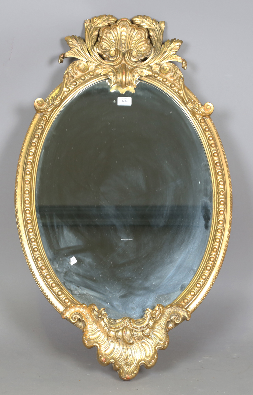 A 20th century rococo style gilt composition oval wall mirror with a shell surmount and scroll