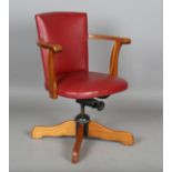 A mid/late 20th century teak framed revolving desk chair, upholstered in claret leather, height