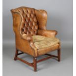 An early/mid-20th century George III style mahogany wing back armchair, upholstered in buttoned