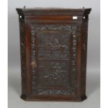 An 18th century provincial oak hanging corner cabinet, the panelled door carved in relief with