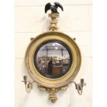A Regency giltwood convex wall mirror with an ebonized eagle surmount above a foliate apron