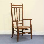 An Edwardian Arts and Crafts oak framed comb back elbow chair with a rush seat, height 109cm,