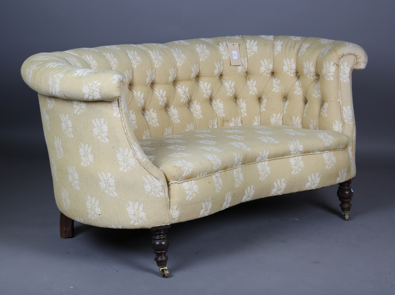 A late Victorian buttoned tub back settee, upholstered in patterned yellow fabric, on turned legs