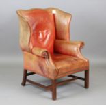 A 20th century George III style shaped wing back armchair, upholstered in faded red leather,