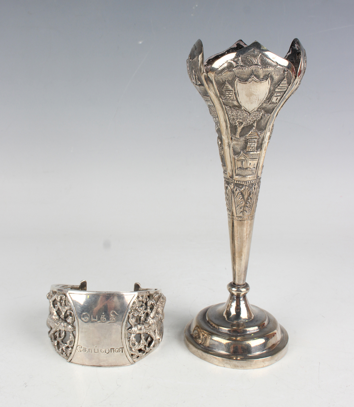 An Indian white metal posy vase, embossed with buildings in landscapes, on a circular foot, height