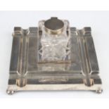 A George V silver square inkstand, fitted with a central cut glass inkwell with silver collar and