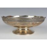 A George V silver circular bowl, pierced with a lattice band beneath a wavy reeded rim, raised on