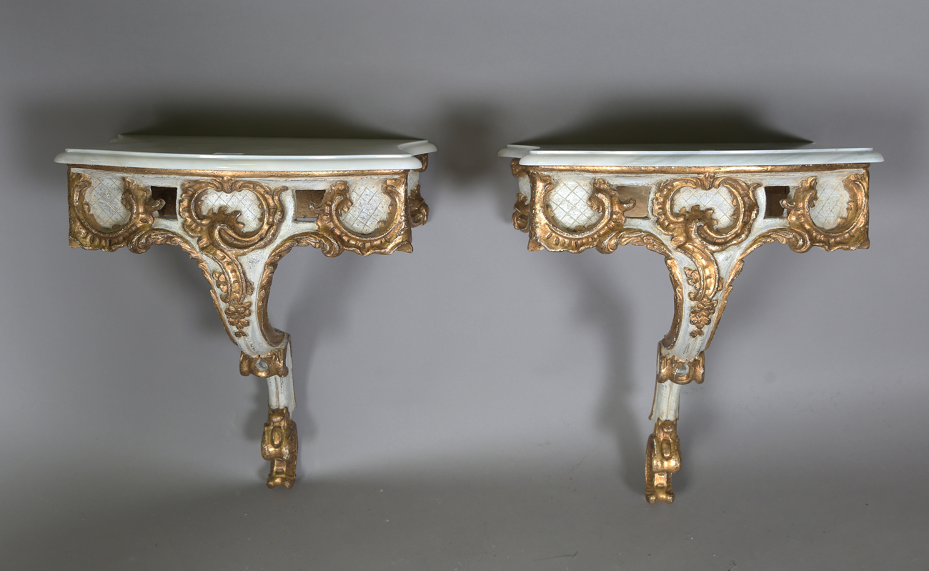 A pair of modern Rococo style white and gilt painted carved wooden console tables with shaped