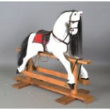 A modern white painted rocking horse, fitted with a leather saddle and raised on an oak stand