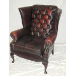 A reproduction wing easy chair upholstered in red buttoned leather on mahogany cabriole legs