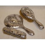 An Edward VII silver three piece dressing set with raised floral decoration comprising hand mirror,