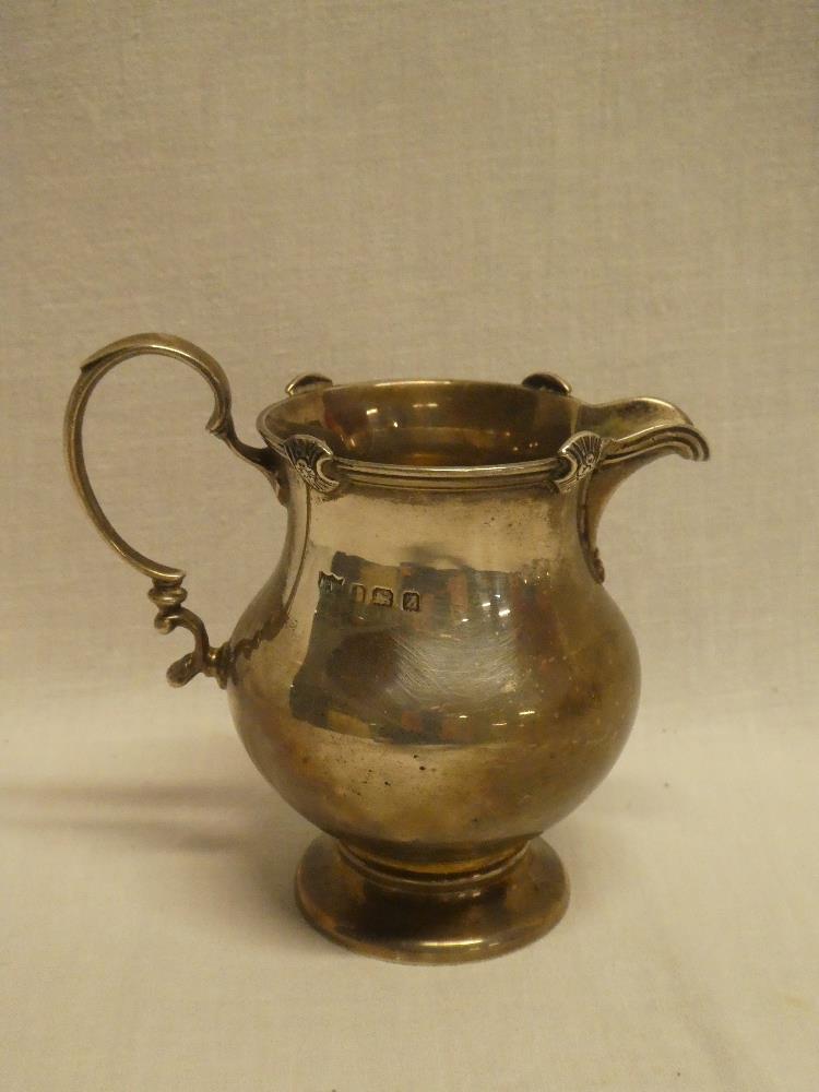 A George V silver baluster shaped cream jug with scroll handle,