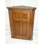 A late 19th century oak hanging corner cupboard with shaped shelves enclosed by a single panelled
