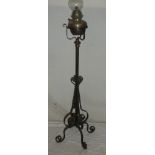 A wrought iron adjustable oil lamp standard supporting a brass oil lamp with glass chimney