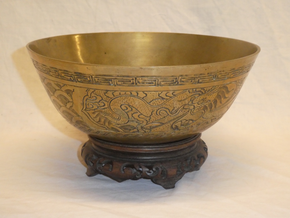 A 20th Century Chinese brass circular bowl with engraved decoration on wooden stand