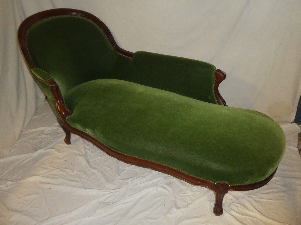 A late Victorian carved mahogany chaise longue upholstered in green fabric with scroll supports on