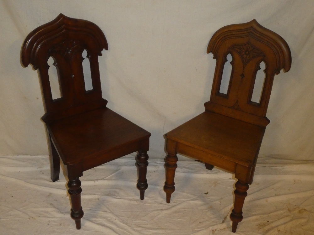 A pair of 19th century carved mahogany hall chairs with pierced backs and polished seats on turned