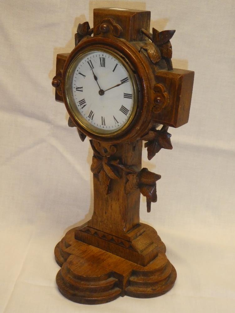 An unusual mantel clock with circular enamelled dial in carved oak crucifix-style case