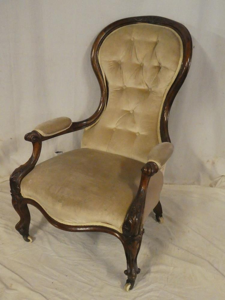 A Victorian carved mahogany open arm easy chair upholstered in buttoned fabric on scroll-shaped