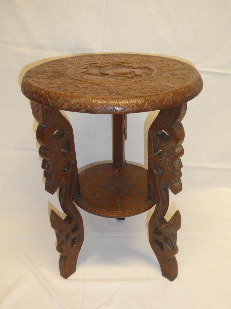 A Burmese carved teak circular two-tier occasional table with animal decorated top on scroll-shaped