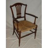 An Edwardian beechwood open arm carver chair with pierced splat back and rushwork seat on turned