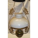 A brass hanging oil lamp with scroll shaped mounts and opaque glass shade