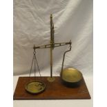 A brass balance scales on rectangular mahogany base and three small brass weights