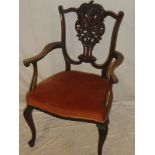 An Edwardian carved mahogany open arm occasional chair with decorated back and upholstered seat on