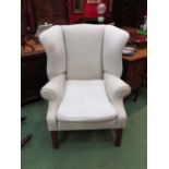 A George III style wing back armchair the scroll arms over reeded square legs joined by stretchers,