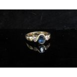 A 9ct gold sapphire and diamond ring the central oval blue sapphire flanked by diamonds in rubover