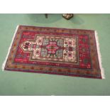 A red ground wool prayer rug with multiple borders, geometric shape to centre, 146cm x 91cm