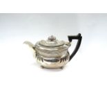 A George III silver teapot embossed curved fluting, gadrooned rim, ball feet and stirrup handle,