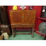 A crossbanded burr walnut two door cabinet on a two drawer barley twist leg stand joined by a "H"