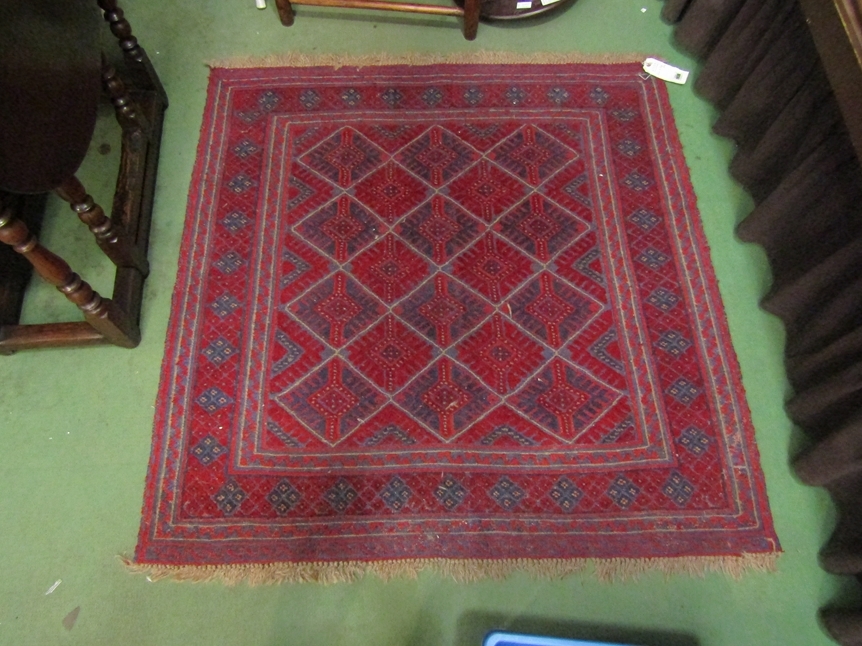 A square rug with diamond geometric patterned centre on red ground with tasselled ends, 125 x 125cm