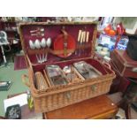 A vintage wicker picnic basket partially filled with original contents, wicker cased syphon, etc