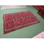 A wool rug, red ground, multiple borders, three central lozenges, tasselled ends, 260cm x 165cm